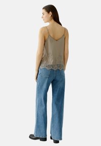 Hellgrau satinierte Camisole mit Spitze am Saum, kombiniert mit weit geschnittenen blauen Denim-Jeans. Verfügt über dünne, verstellbare Träger und ein V-förmiges Rückendessin.