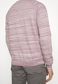 Maglione leggero color bordeaux con strisce orizzontali, polsini e orlo a coste, scollo rotondo e vestibilità comoda. Tessuto texturizzato.