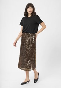 Pronksist sequins, midi-seelik külgsuuga, koos musta puuvillase T-särgi ja mustade kontsapededega. Sile tekstuur ja läikiv pind.