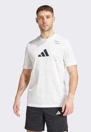 Vit t-shirt med kort ärm som har en stor svart Adidas-logga och textdetaljer. Tillverkad av mjukt tyg, med en enkel, sportig design.