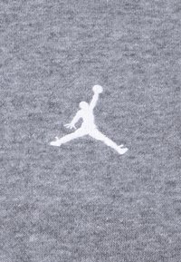 Pelēks auduma T-krekls ar baltu izšūtu jumpman logotipu. Mīksta tekstūra un ikdienišķs dizains, piemērots sportiskai vai ikdienas valkāšanai.