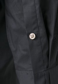 Black textile garment featuring a decorative metallic button with a star design. Smooth texture, with subtle stitching details.