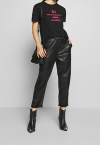 Czarny graficzny t-shirt z różowym napisem, połączony z czarnymi spodniami tapered z ekoskóry i stbootami z ćwiekami. Torebka na ramię również w kolorze czarnym.