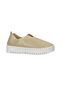 Zapatos beiges tipo slip-on con parte superior perforada, suela blanca texturizada y un diseño plano. Presentan una pequeña pestaña en la parte trasera para facilitar el calzado.