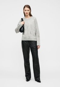 Donna che indossa un maglione lavorato a maglia grigio chiaro, pantaloni larghi neri con trama, scarpe nere con punta e tiene una borsa a tracolla nera.