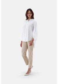 Weiße bestickte Bluse mit Knopfverschluss und Ballonärmeln, kombiniert mit beigen Slim-Fit-Hosen und cremefarbenen Schuhen.