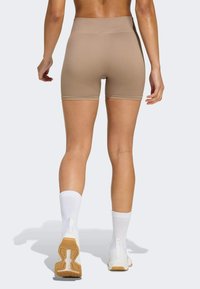 Person from behind wearing beige high-waisted biker shorts, white crew socks, and white athletic shoes with gum soles on a light background.