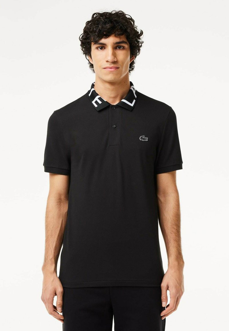 Schwarzes Polohemd mit einem gemusterten Kragen, der weiße Buchstaben trägt, kurzen Ärmeln und einem kleinen Logo auf der Brust. Schlichte Textur.