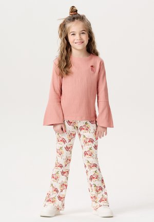 Top rosa con texture, maniche a campana e dettagli ricamati, abbinato a pantaloni a palazzo con motivo floreale in crema e sneaker bianche.