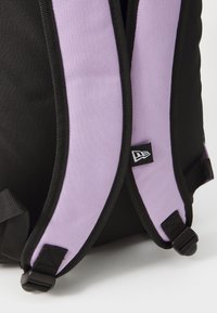 Black backpack featuring padded lavender straps, black trim, and an adjustable buckle. Includes a small logo tag on one strap.