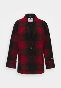 Czerwony i czarny płaszcz w kratę z kołnierzem w stylu szala, zapinany na jeden guzik, z bocznymi kieszeniami. Tkanina wydaje się miękka, o szczotkowanej fakturze.