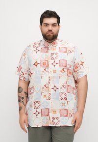 Chemise à manches courtes avec un motif patchwork composé de carrés rouges, bleus et crème, motifs floraux et un col classique.