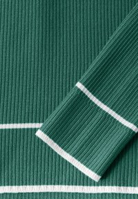 Grüner gerippter Stoff mit weißen Streifen am Halsausschnitt und an den Ärmeln. Die Textur ist gestrickt und hat eine glatte Oberfläche.