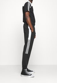 Black athletic outfit with white accents; t-shirt has a color-block design, and pants feature side stripes. Paired with black high-top sneakers.