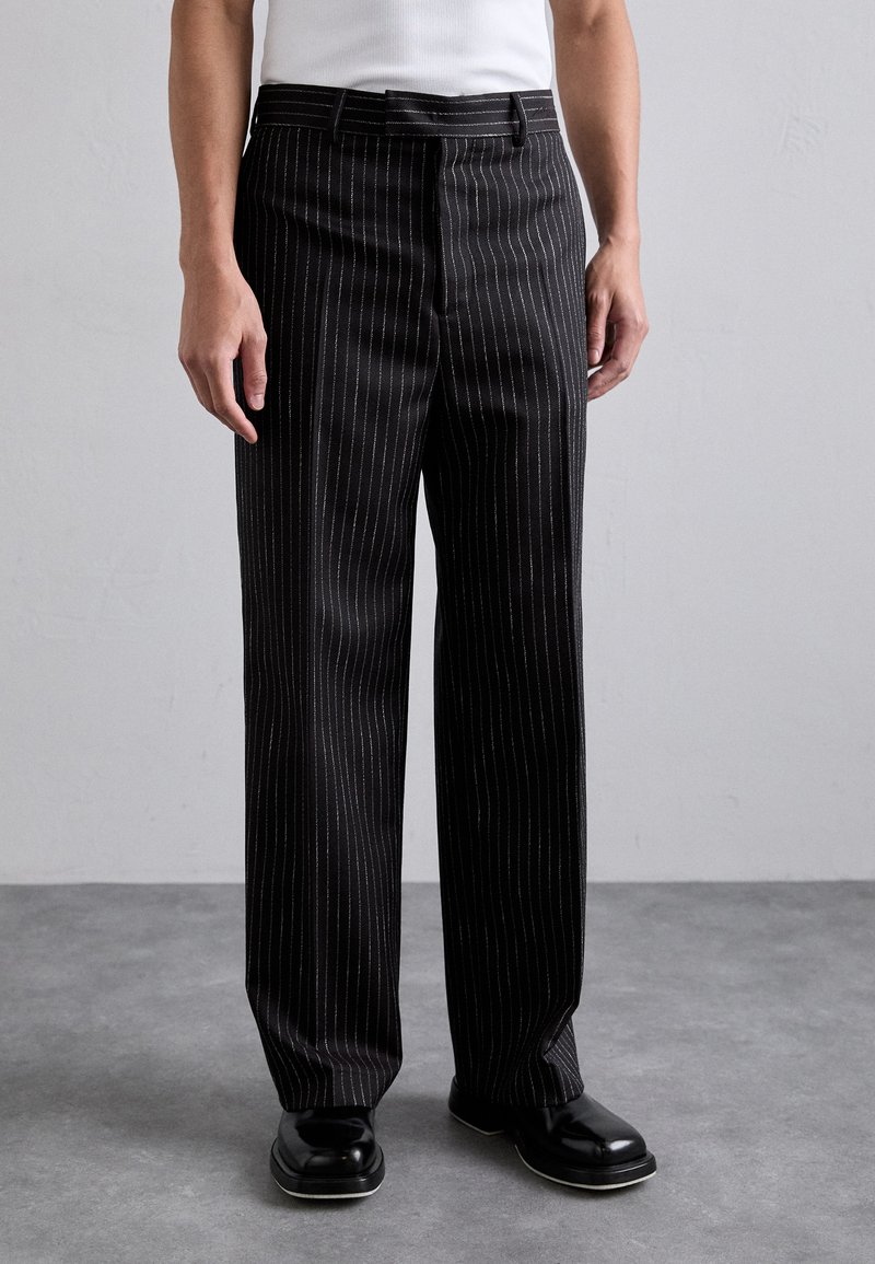Black pinstripe trousers with a tailored fit, featuring a smooth texture and a flat front, paired with black shoes.