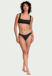 Must mustriga komplekt, millel on ruudukujuline kaelus ja laiad rihmad, ning madala taljega hipsteri püksikud. Sile tekstuur, minimalistlik disain, ilma mustriteta.