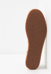 Semelle d'une chaussure beige avec un texte en relief répété de "Tommy Hilfiger" sur un fond blanc uni.