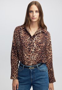 Blouse met luipaardprint en kraag, gemaakt van een gladde stof, met lange mouwen en een losse pasvorm, gecombineerd met blauwe spijkerbroek en een riem.