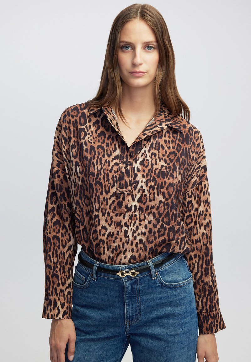 Blouse met luipaardprint en kraag, gemaakt van een gladde stof, met lange mouwen en een losse pasvorm, gecombineerd met blauwe spijkerbroek en een riem.