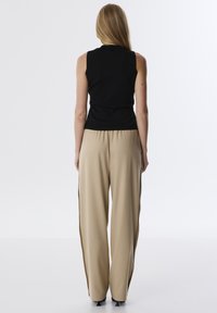 Top nero senza maniche abbinato a pantaloni beige a gamba larga, con pinces e una vestibilità rilassata, caratterizzati da una texture di tessuto liscia.