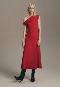 Vestido rojo de un solo hombro con tela drapeada, corte a la altura de la rodilla y textura suave, combinado con botas altas de tacón negras.