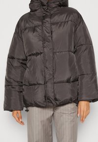 Chaqueta de plumón en gris oscuro, con capucha, diseño acolchado y un corte holgado. Textura suave con detalles de ajuste en el dobladillo y los puños.