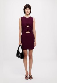 Burgundy sleeveless dress with cutout details, featuring accent hardware, paired with a black handbag and strappy sandals, smooth fabric.