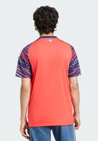 Rood sportshirt met marineblauwe gestreepte mouwen, voorzien van korte mouwen en een rechte snit. Stof lijkt licht en ademend te zijn.