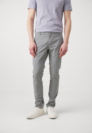 Pantaloni di cotone grigio chiaro slim fit, con tasche frontali e passanti per cintura. Abbinati a sneakers bianche e a una t-shirt viola chiaro.