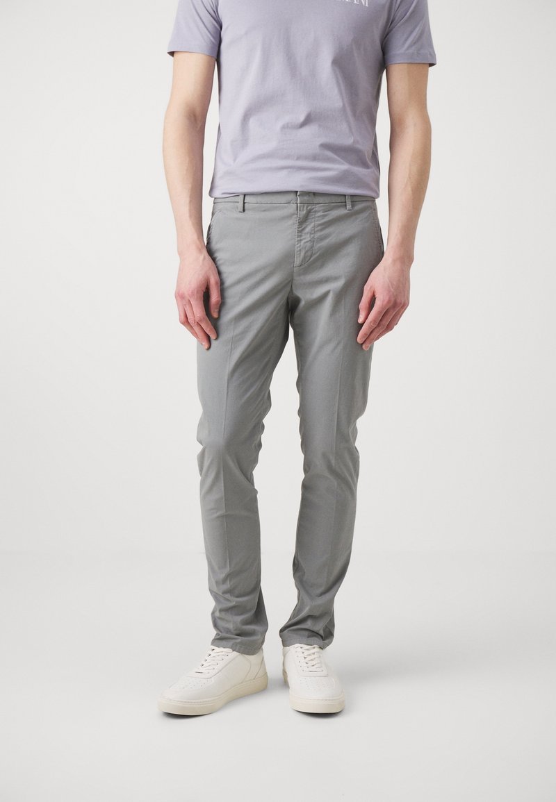 Pantaloni di cotone grigio chiaro slim fit, con tasche frontali e passanti per cintura. Abbinati a sneakers bianche e a una t-shirt viola chiaro.