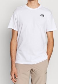 Bílé bavlněné tričko s klasickým výstřihem a krátkými rukávy. Na levé straně hrudi se nachází malé černé logo "The North Face".
