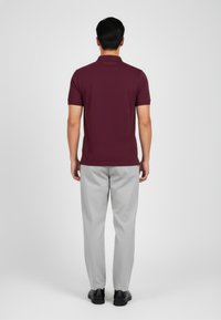 Bordová polo košile s krátkým rukávem, spárovaná se světle šedými kalhotami. Černé boty dotvářejí celý outfit. Materiál vypadá hladce a lehce.