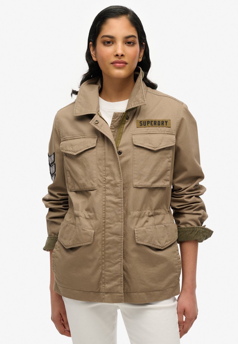 Lichtbruine militaire stijl jas van stof met vier voorzakken, een verstelbare taille en een "Superdry" logo op de borst.