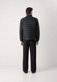 Zwarte gewatteerde pufferjas met een hoge kraag en elastische manchetten, gestyled met lose zwarte broek. Gladde textuur en minimalistisch ontwerp.