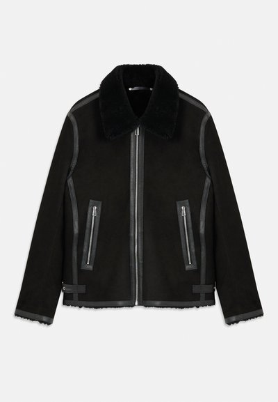 Svart shearlingjacka med bred pälskrage, framzipper, fickor med dragkedja på sidan och läderdetaljer på sömmarna och ärmsluten.