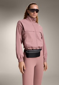 Könnyű, rózsaszín dzseki magas gallérral, hozzá illeszkedő rózsaszín leggings és egy fekete deréktáska cipzáras zsebbel. Sötét napszemüveg.