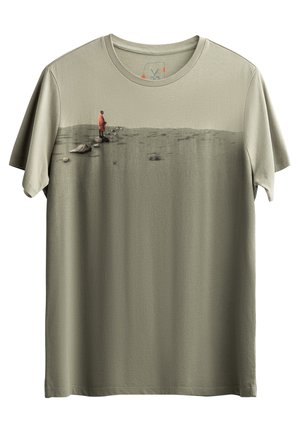 T-shirt in cotone verde oliva con una stampa grafica di una figura in un cappotto rosso che si erge su un paesaggio testurizzato. Maniche corte, collo rotondo.