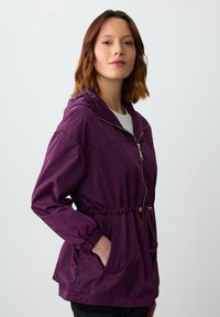 Lila lichtgewicht capuchonjack met elastische tailleband, voorzakken en een volledige ritssluiting. Gladde textuur en casual ontwerp.
