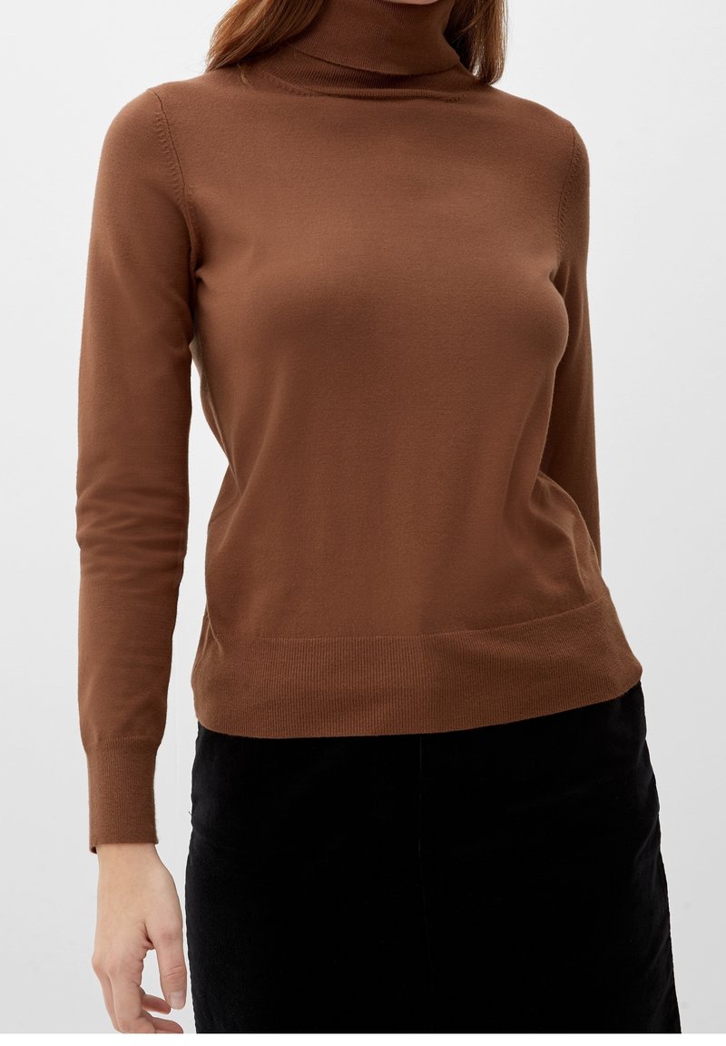 Brauner Rollkragenpullover mit langen Ärmeln, weichem Material, taillierter Passform und Rippdetails am Kragen und Saum. Kombiniert mit einem schwarzen Rock.