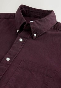 Burgunderfarbendes Button-up-Hemd aus Baumwolle, ausgestattet mit einem klassischen Kragen, weißen Knöpfen und einer linken Brusttasche. Strukturierter Stoff mit lässiger Passform.