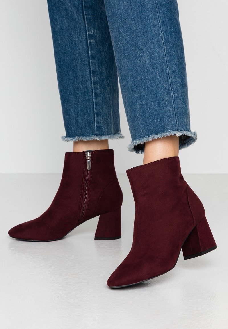 Burgundy suede nilkkurit terävällä kärjellä, lohkokorkealla ja sivuvetoketjulla; siinä on sileä pinta ja minimalistinen muotoilu.
