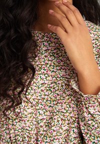 Haut à motif floral aux couleurs pastel, avec des détails roses et verts. Tissu doux avec un design fluide et des poignets froncés aux manches.