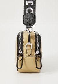 Malá béžová kožená crossbody taška so striebornými zipsami, čiernym popruhom a kovovými detailami. Má obdlžníkový tvar a dva ťaháky na zips.