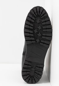 Svart gummistövelsula med djupa mönster och ett zigzag-mönster, med en slät kant och en rektangulär inskärning på ytan.