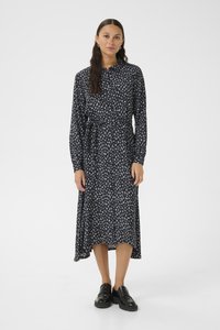Navyblaues Langarmkleid mit floralem Muster, fließendem Stoff und gebundenem Taillenbereich. Kombiniert mit schwarzen Schuhen und einem schlichten Ohrring.