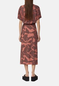 Maxi-jurk in roestkleur met abstract bruin patroon, korte mouwen en een ontspannen pasvorm. Gecombineerd met dikke zwarte platform schoenen.