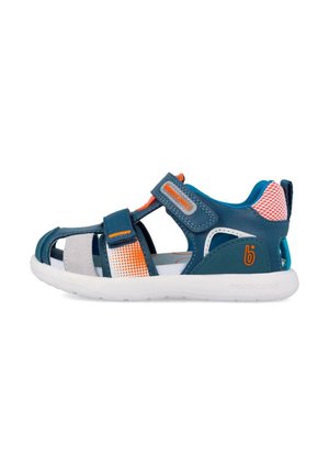 Sandalia abierta para niños en azul marino y naranja con correas ajustables de velcro y suela blanca acolchada, vista lateral.