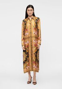 Μακρύ φόρεμα με κουμπιά σε χρυσό χρώμα, με λουλουδένια και γεωμετρικά σχέδια σε ροζ, μαύρο και κρεμ. Λείο ύφασμα με ίσια γραμμή και μακριά μανίκια.