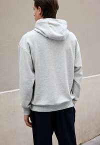 Grey hoodie made of soft, textured fabric, featuring a kangaroo pocket and a drawstring hood. Loose fit and ribbed cuffs at the hem.