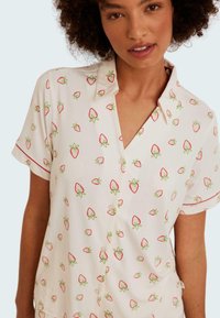 Kortärmad skjorta i mjuk vit tyg, med ett jordgubbsmönster i röd och grön, med knäppning fram och krage.